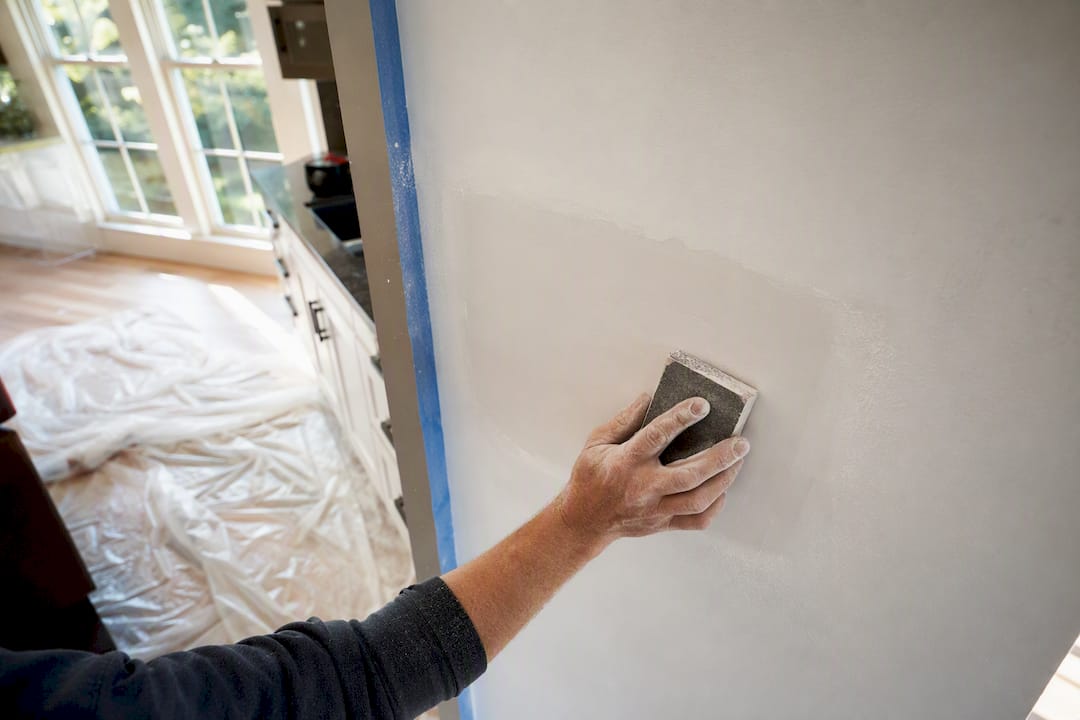 Hands sanding feathered edges of wall patch