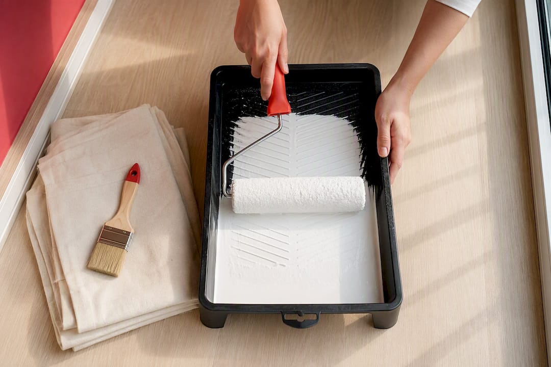 Hands loading a paint roller in tray